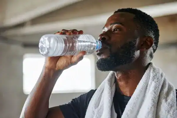 Image of man drinking water to improve hydration Reigate after work out.